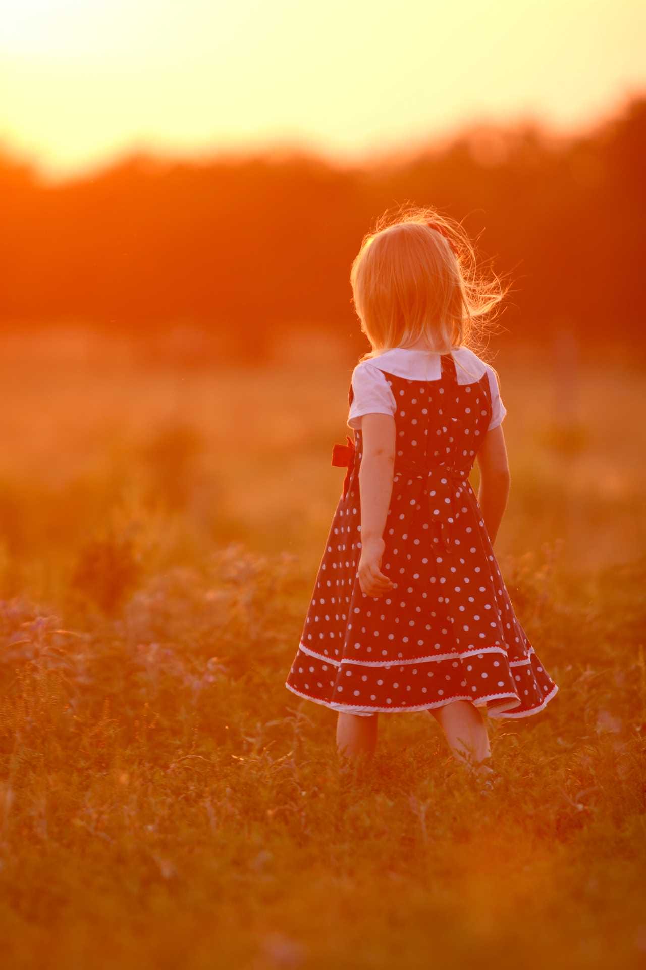 A little girl in a polka dot dress walking in a field at sunset.