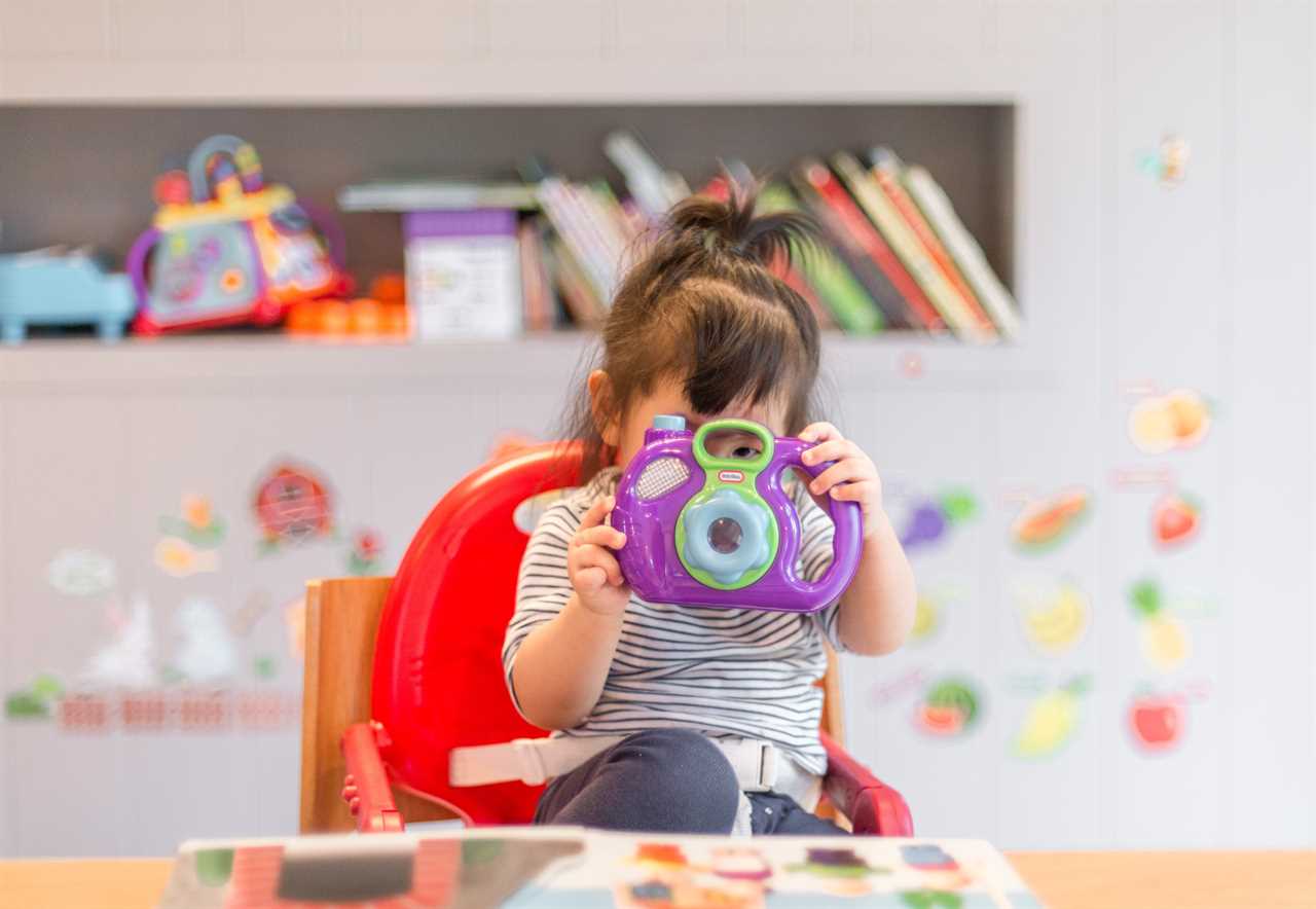 A little girl in a high chair taking a picture with a camera.