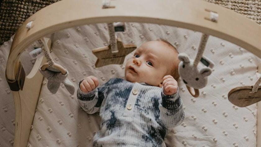 A baby is laying on a wooden cradle.