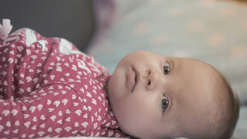 A baby laying on a bed looking at the camera.