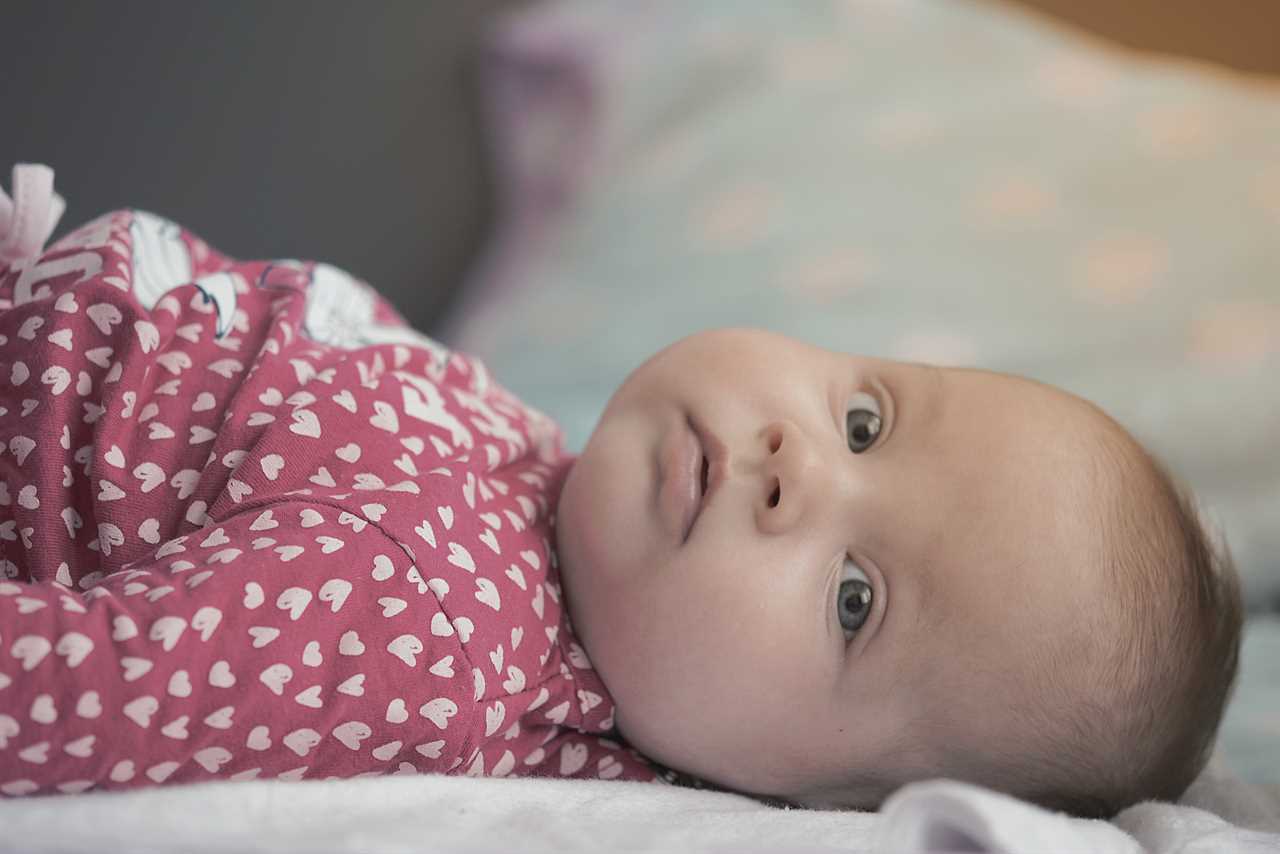 A baby laying on a bed looking at the camera.