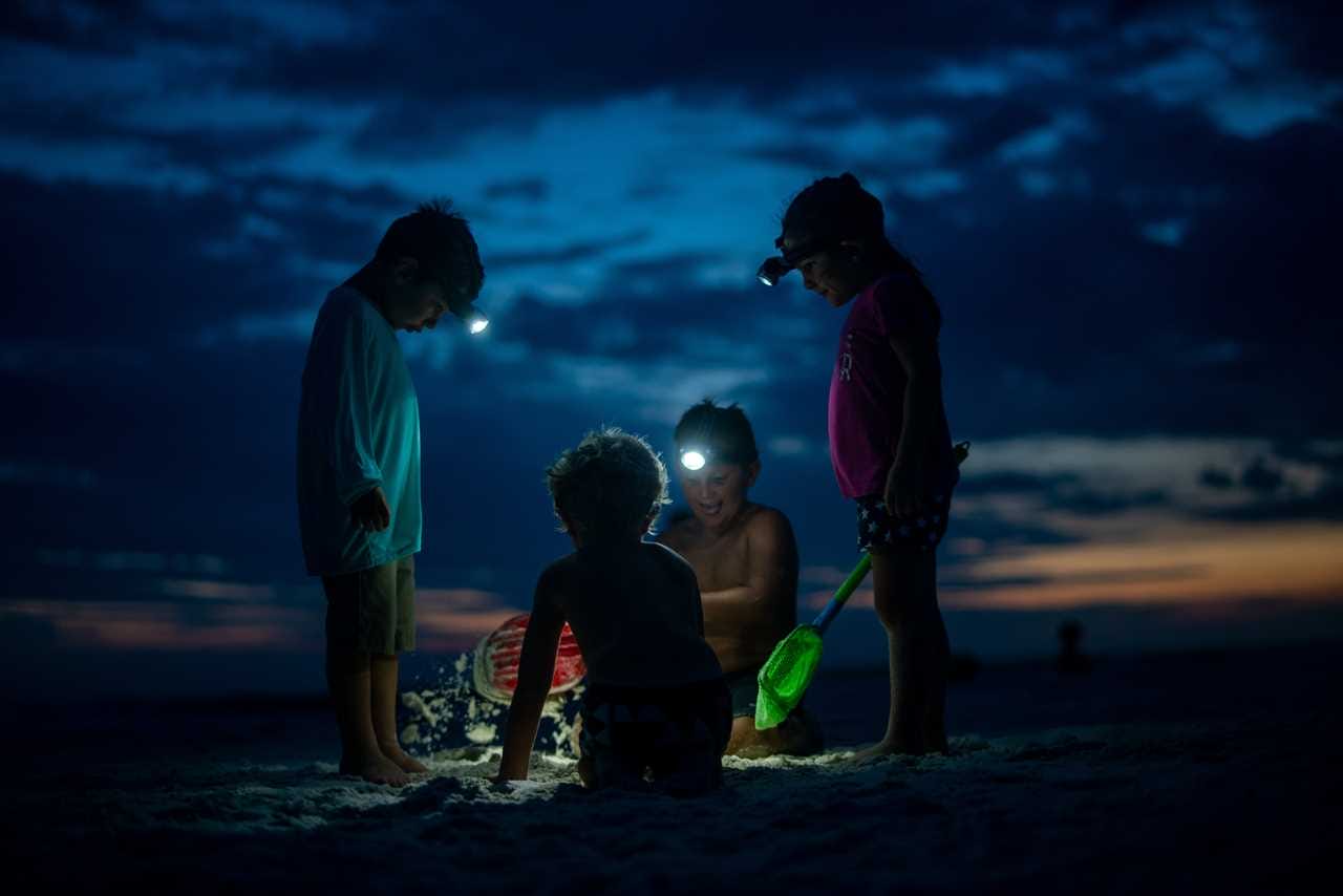 Three children playing in the sand at night.