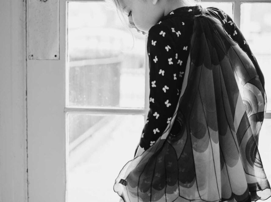 A little girl in a black and white photo standing in front of a door.