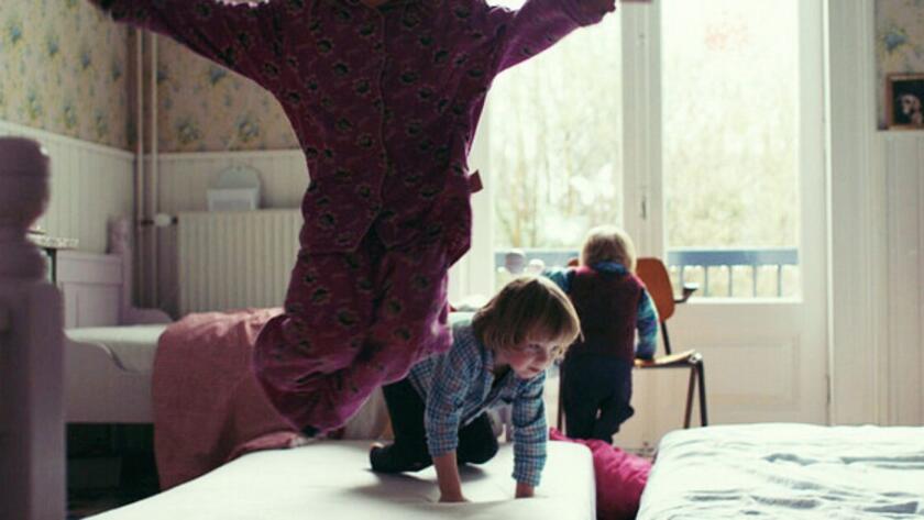 Child performing a handstand on a bed with another child watching in the background.