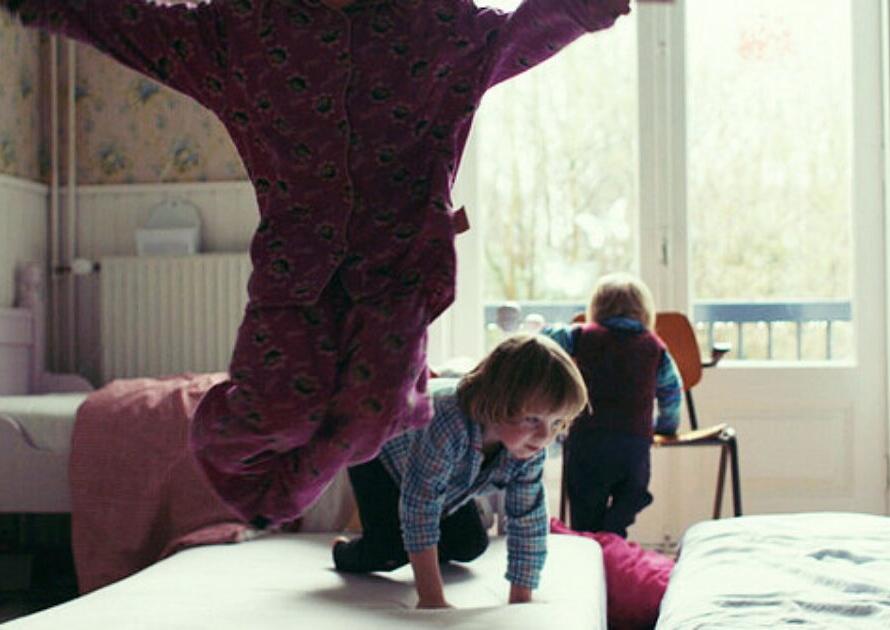 Child performing a handstand on a bed with another child watching in the background.